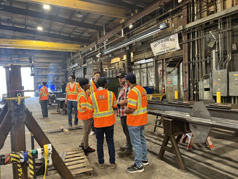 Students wearing PPE talk to employees about metal fabrication.