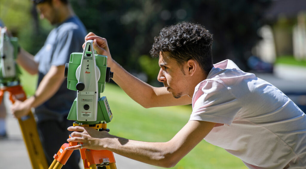 Student works with surveying equipment out in the field.