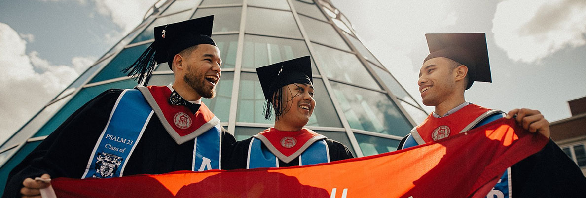 Three WSU students wearing caps and gowns and holding a Cougar flag.