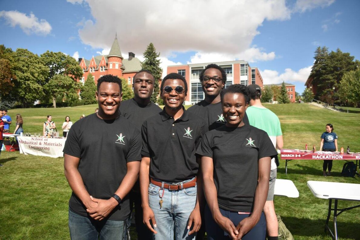 Four black engineering students pose by their National Society for Black Engineers booth.