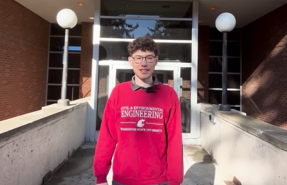 Student wearing a WSU sweatshirt in front of glass doors to a building.