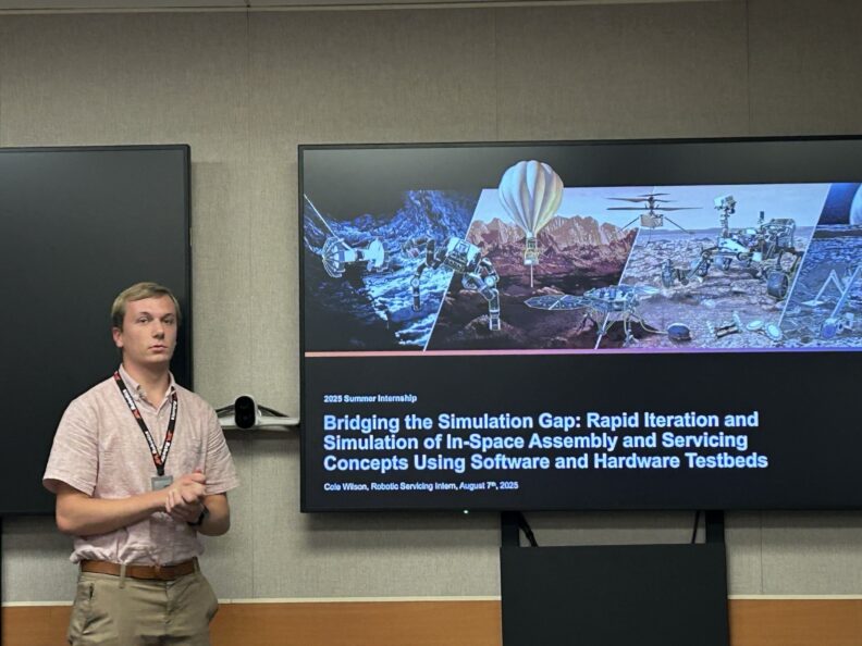 man standing next to a TV screen showing test models used in space exploration.