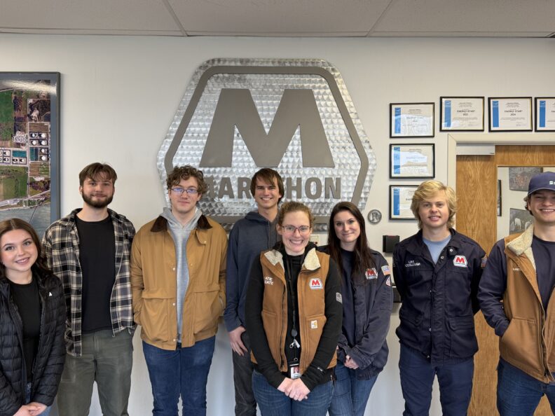 students standing infront on a marathon sign.