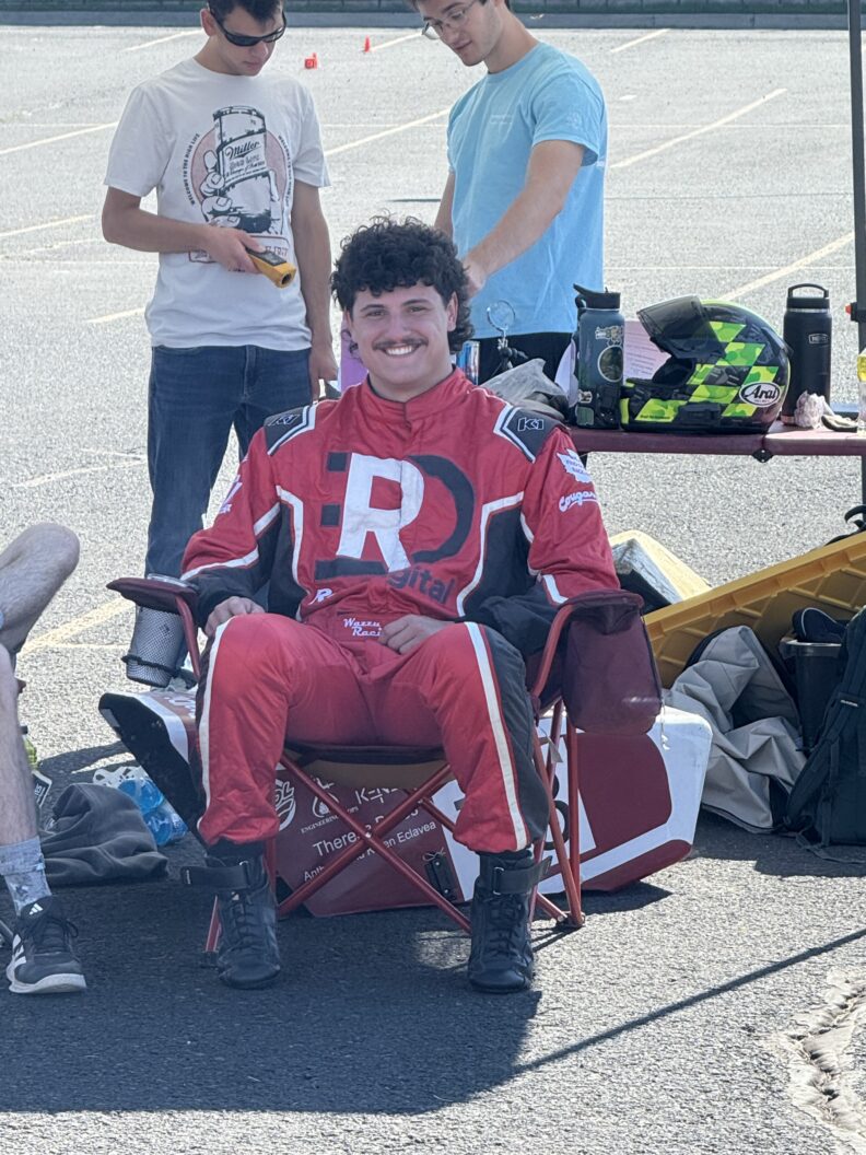 A man in a red racing suit sitting in a camping chair.