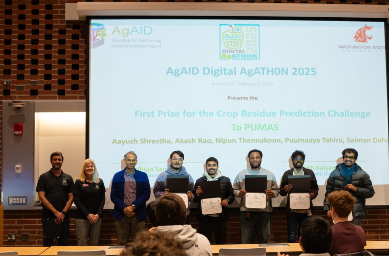 A group of people with students holding certificates in front of a projector screen.