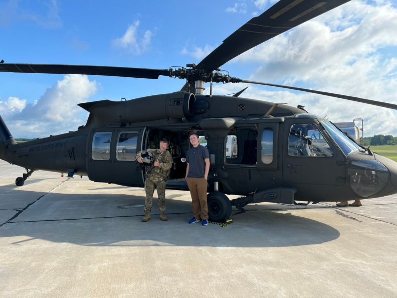 two people, one of them dressed in Army uniform, standing in front of a U.S. Army helicopter.