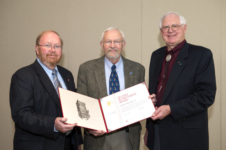 Three men posing with an award.