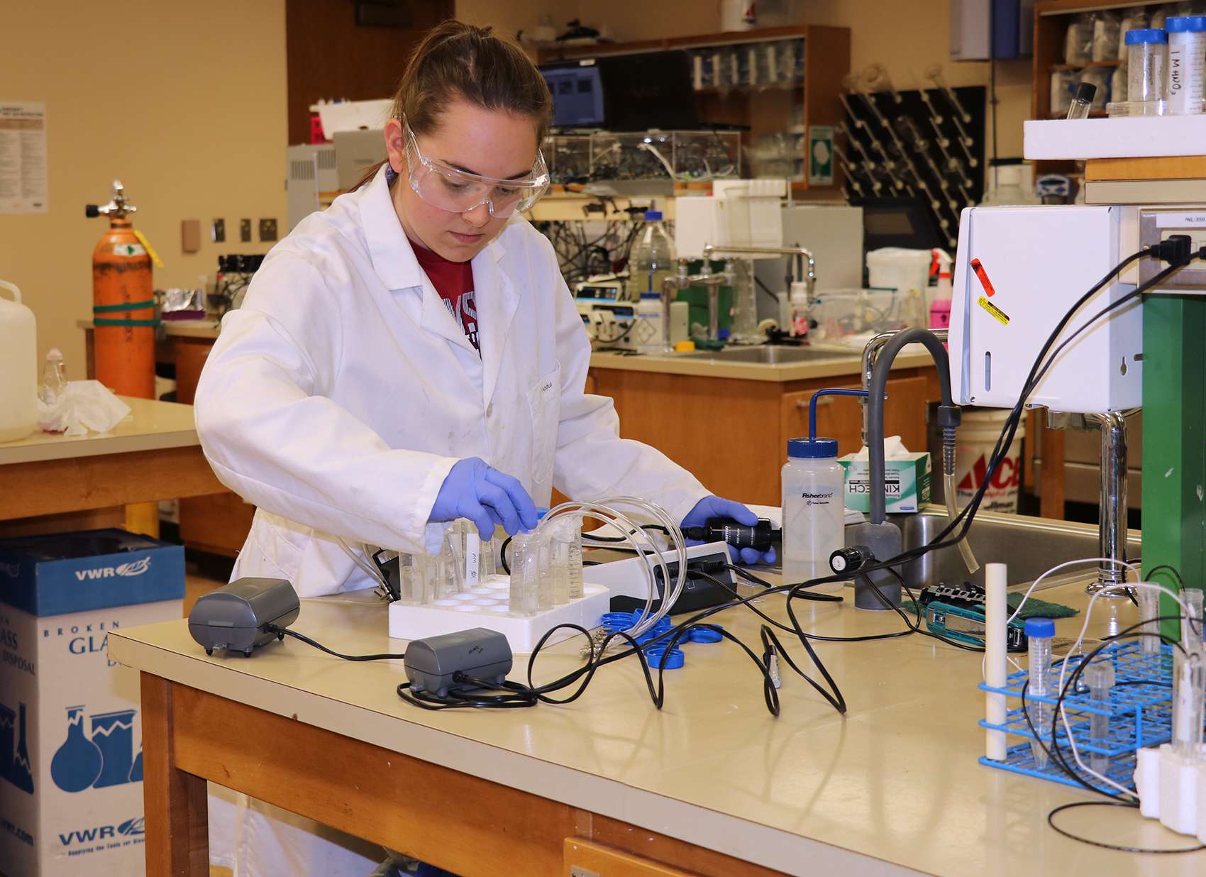 Student in lab coat working with vials of chemicals and other equipment.