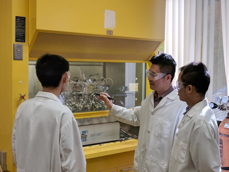 Three people wearing white lab coats in a lab.