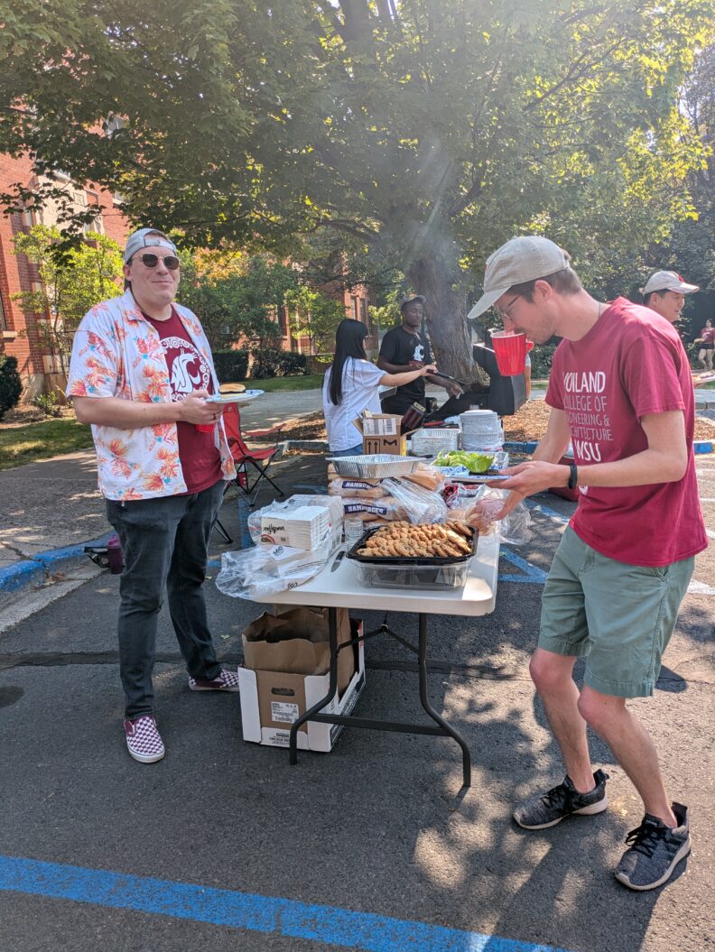 People filling their plates at an outdoor buffet table.