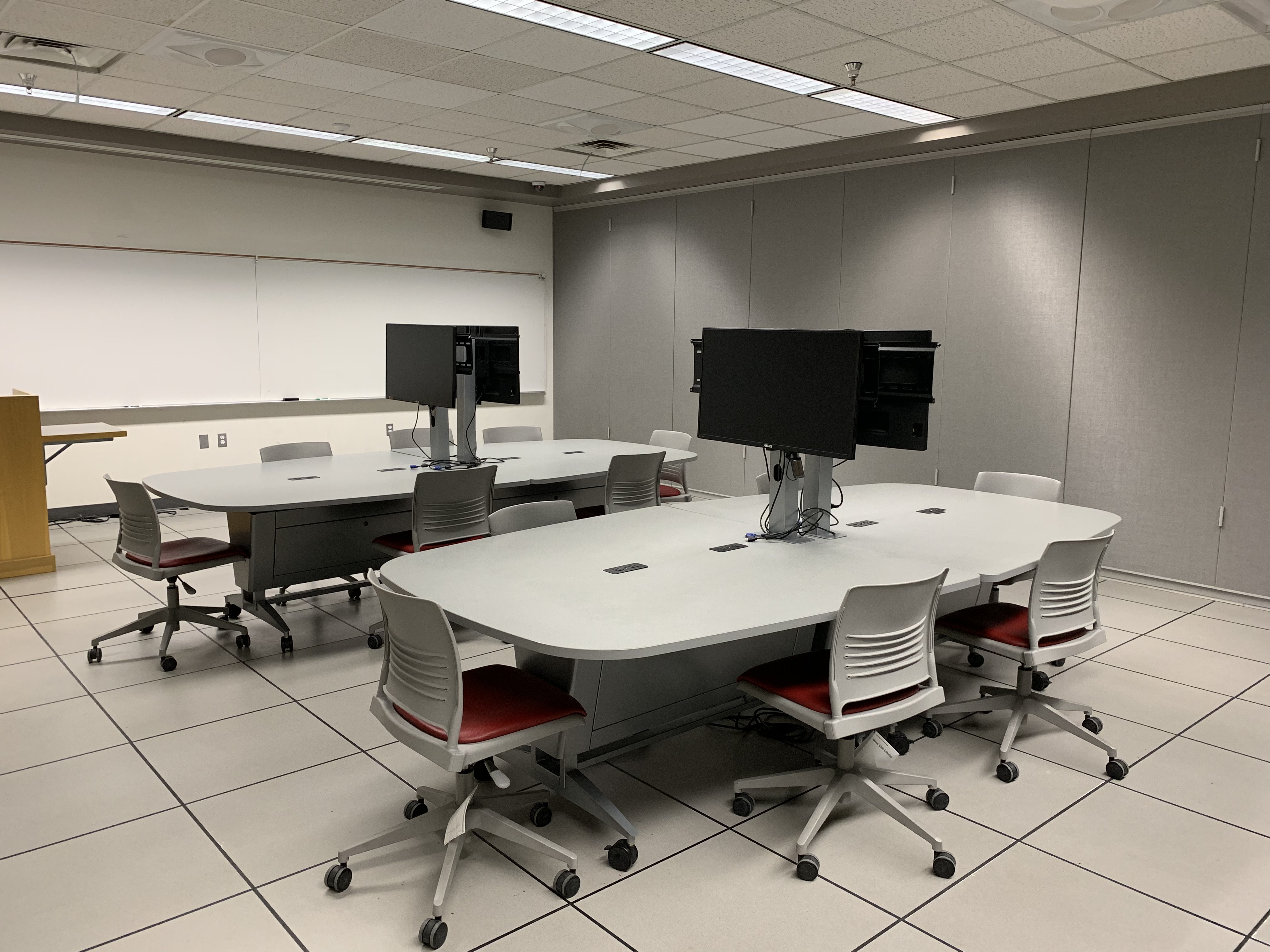 The pictured room contains several meeting tables, chairs and monitors at the center of the table.