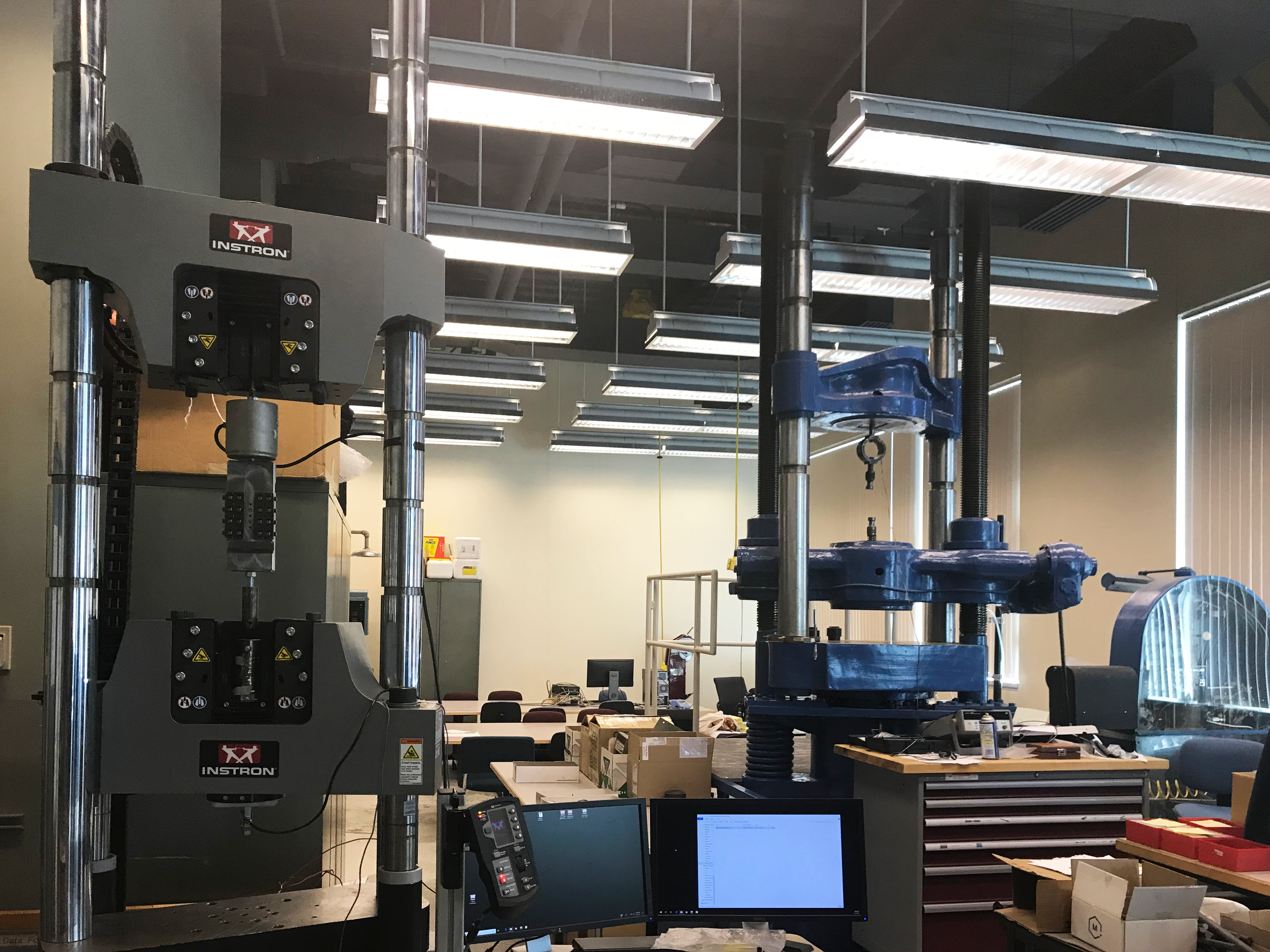 The image shows two tensile testing machines as well as other material and mechanical equipment being used in the lab.