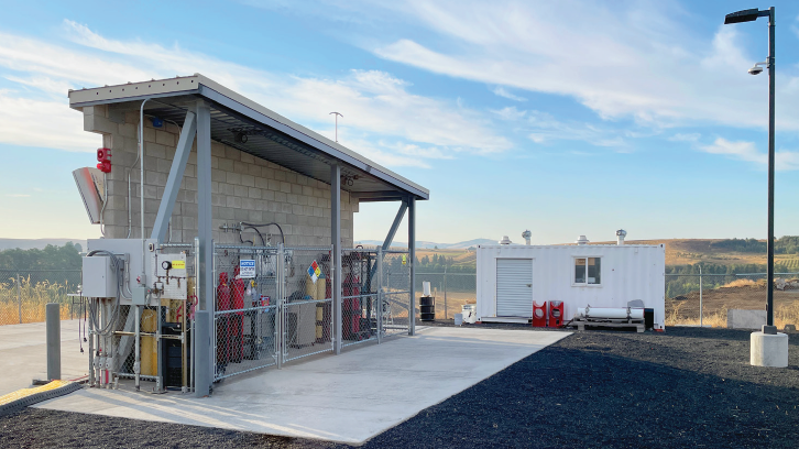 a white office trailer near a lean-to sheltering gas cylinders that is enclosed by chainlink fencing.