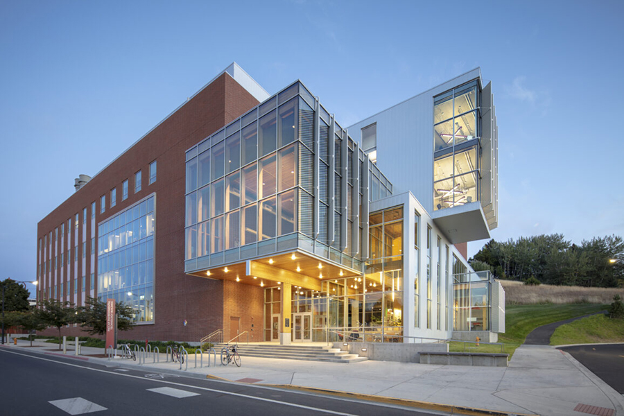Exterior view of a sharply angled, multistory brick and glass building at dusk.