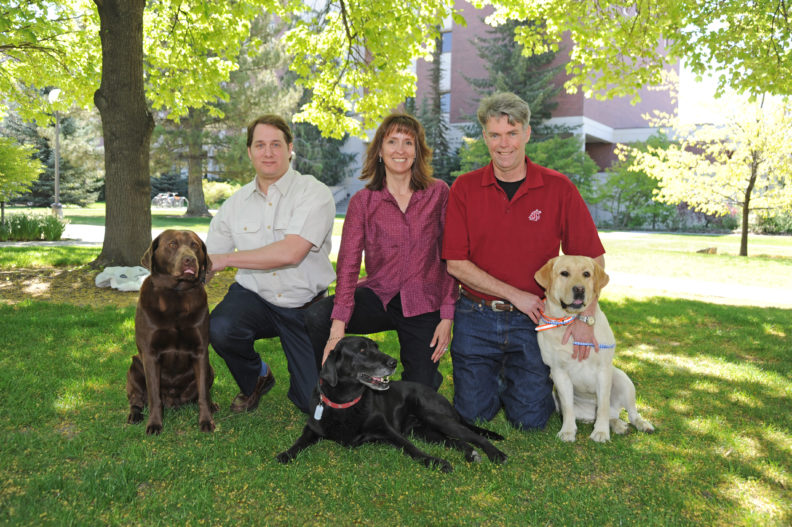 Nicolas Villarino with a chocolate lab, Katrina Mealey with a black lab, Michael Court with a yellow lab