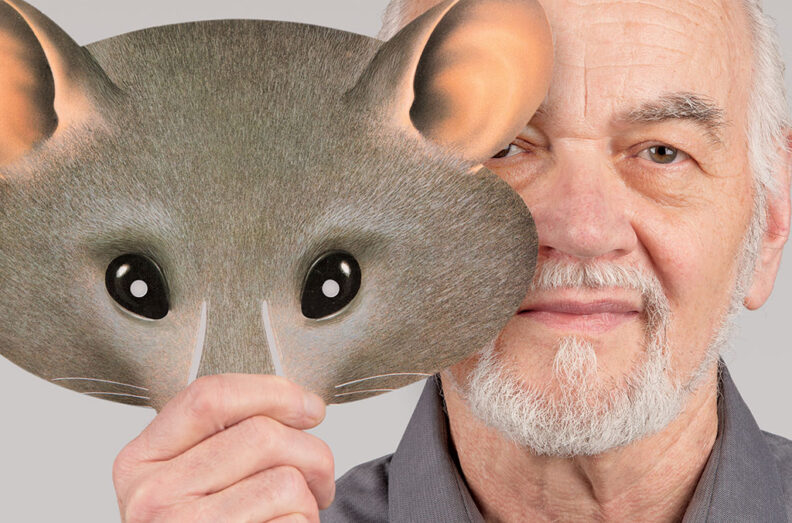 Close up of Jaak. He is holding a mask of a rat that partially covers his face.