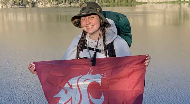 Trinity Wood holding a WSU flag while on a hike.