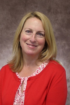 Professional headshot in the studio. She is wearing a red sweater over a red and white patterned top.