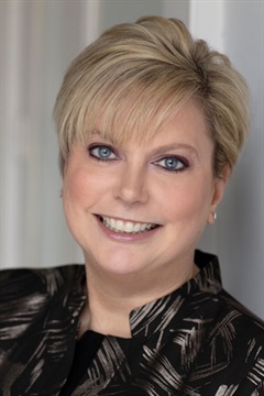 Tightly cropped professional headshot of Stacy. She's wearing a black and gray patterned top.