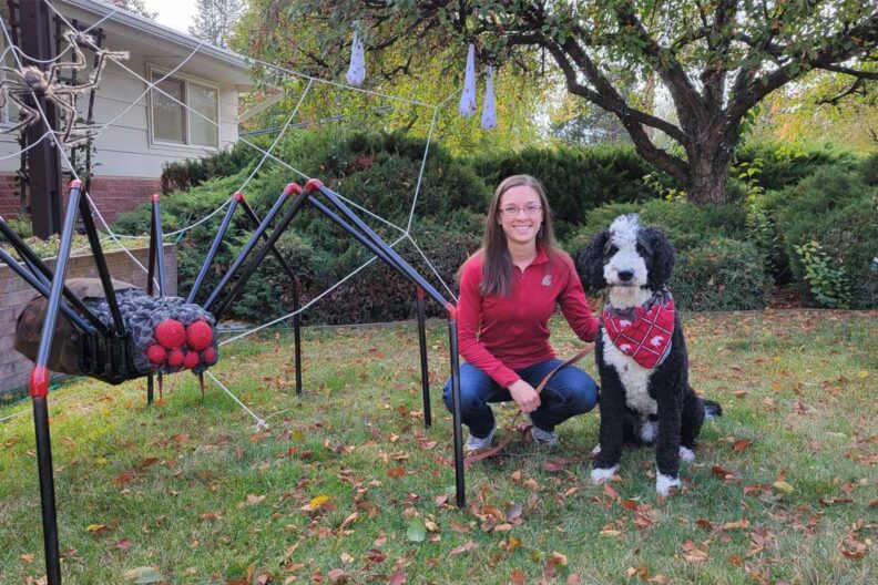 Emily and her dog in her front yard that is decorated with a giant spider for Halloween.