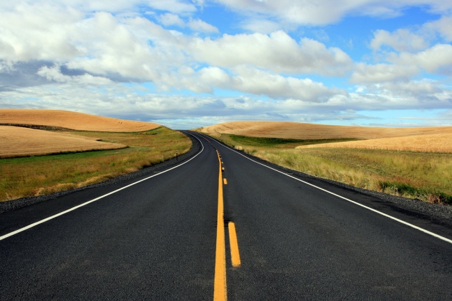 Freshly striped 2-lane blacktop highway running through a harvested wheat countryside.