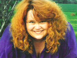 Close up photo of Norma. She has curly long red hair and is wearing a purple shirt.