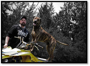 Photo of man with his dog standing on a yellow 4-wheeler.