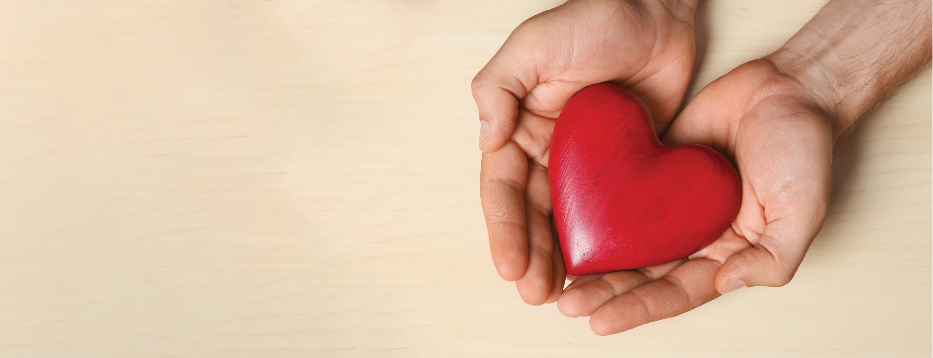 Staged photo of a person's hands cupping a small wooden heart.