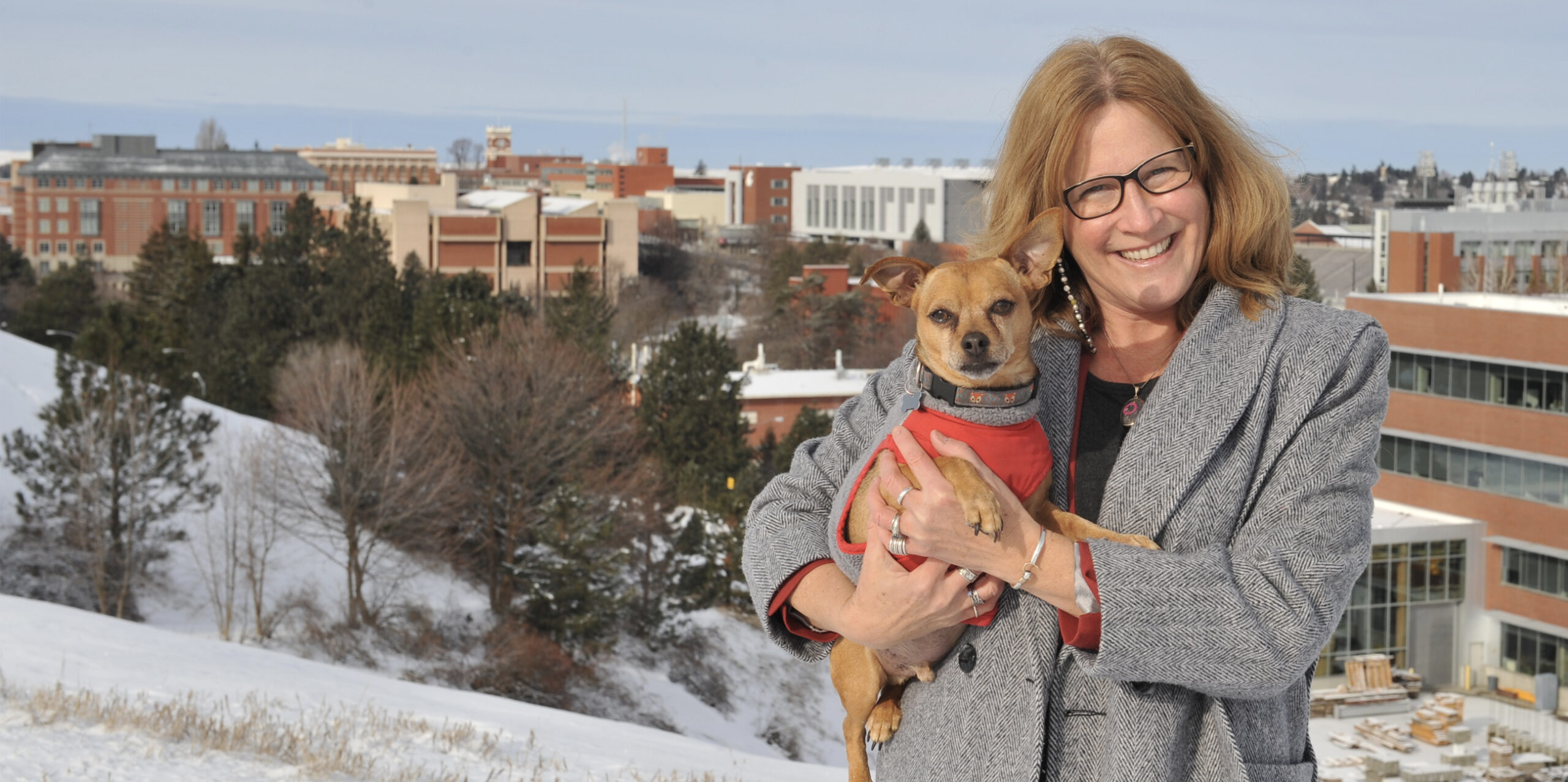 Dean Dori Borjesson standing on the hill overlooking the College of Veterinary Medicine. It is winter and she is holding her small dog.