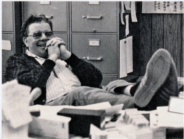 Dr. Farrell at his desk, feet up on the desk and his hands clasped in front of him. He's smiling.