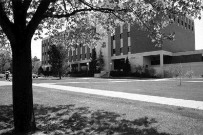 Black and white photo of Bustad Hall in 1985. The grassy area in front of it only has a few large trees.