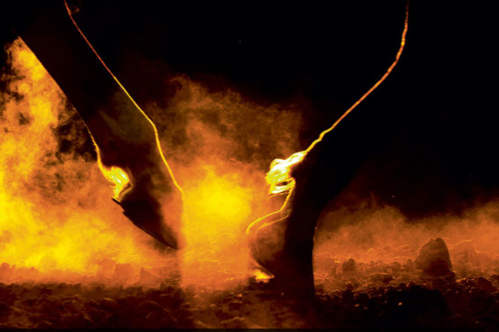 Close up image of a horse's hooves as it walks in dirt, stirring up dust.