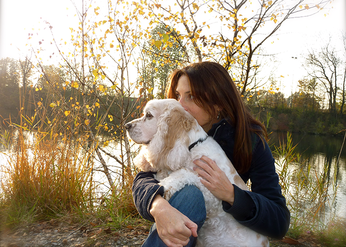 Woman with her dog on the edge of a pond or river in autumn.