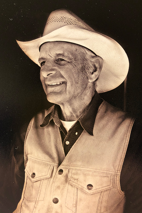 Sepia image of John James "Kicker" Curtis. He's wearing a dark shirt, light vest and a cream cowboy hat.