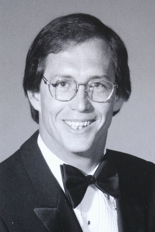 Studio photo of Thomas. He is wearing a black suit, white shirt, and black bowtie.