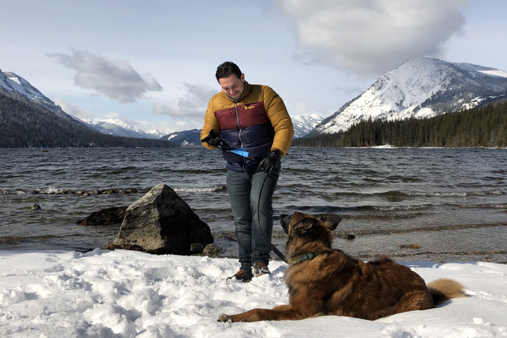 Carlos on the edge of a mountain lake in the winter, with a dog at his feet.