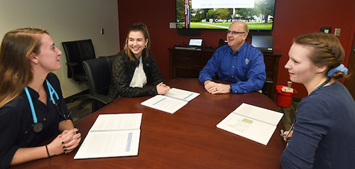 Dr. Debowes with three students in a conference room.