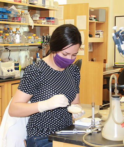 Floricel in a lab. Dressed in plain clothes, but wearing a mask and gloves.