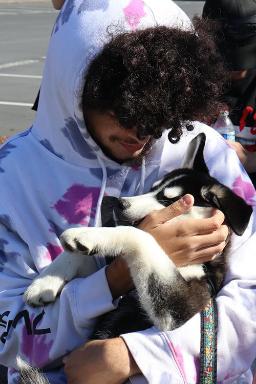 A young man in a colorful hoodie holds his husky pup in his arms like a baby.
