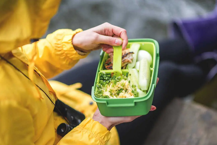 Person eating their lunch out of a plastic container, and with a plastic spoon.
