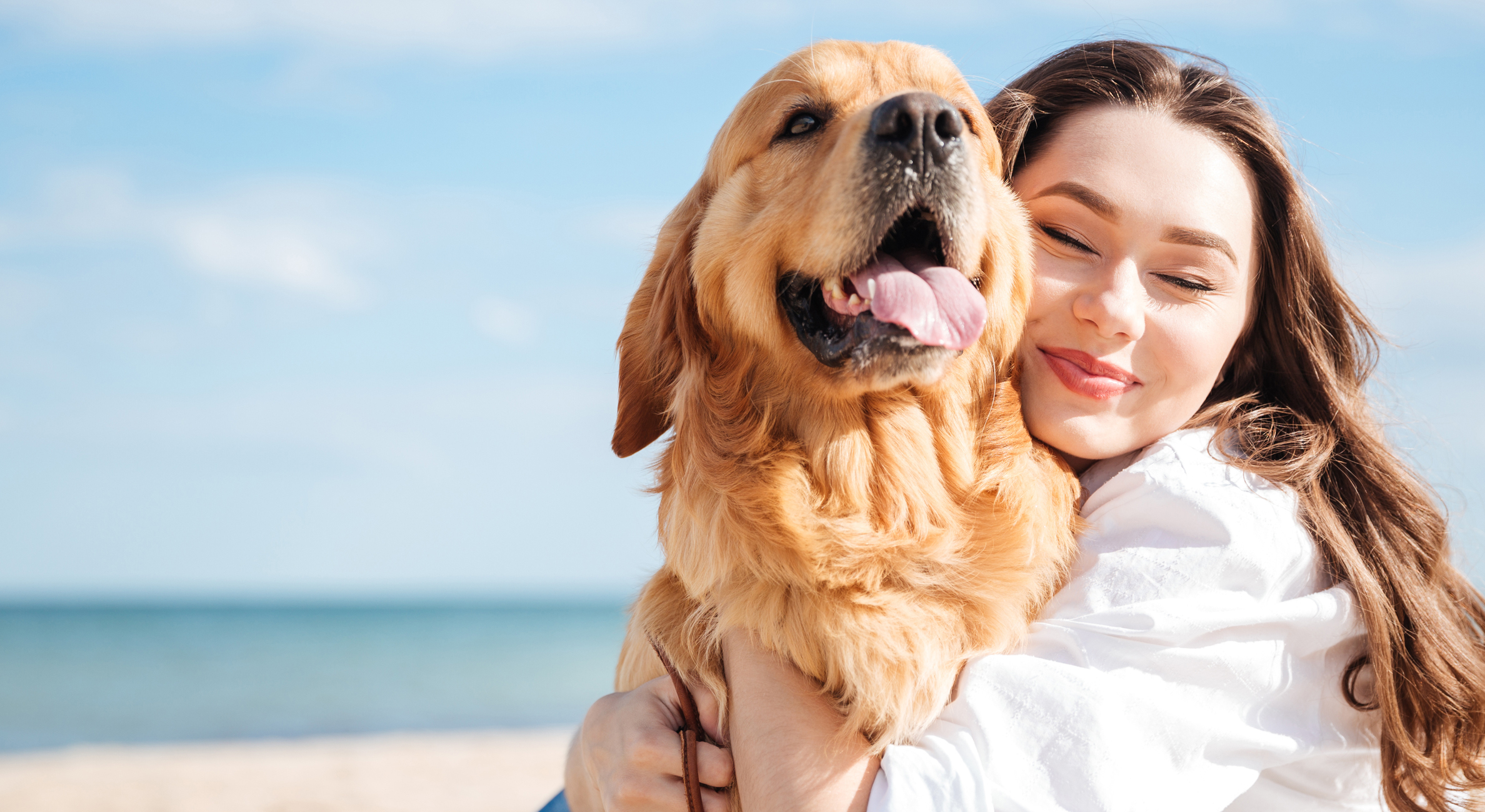 Close up shot of a young person hugging a large Golden Retriever while on a beach.