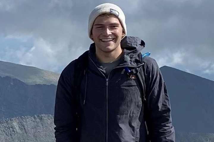 Peyton on a hiking trip with a mountain range behind him.