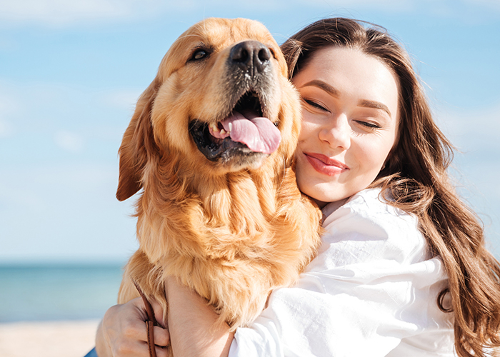 Close up shot of a young person hugging a large Golden Retriever while on a beach.