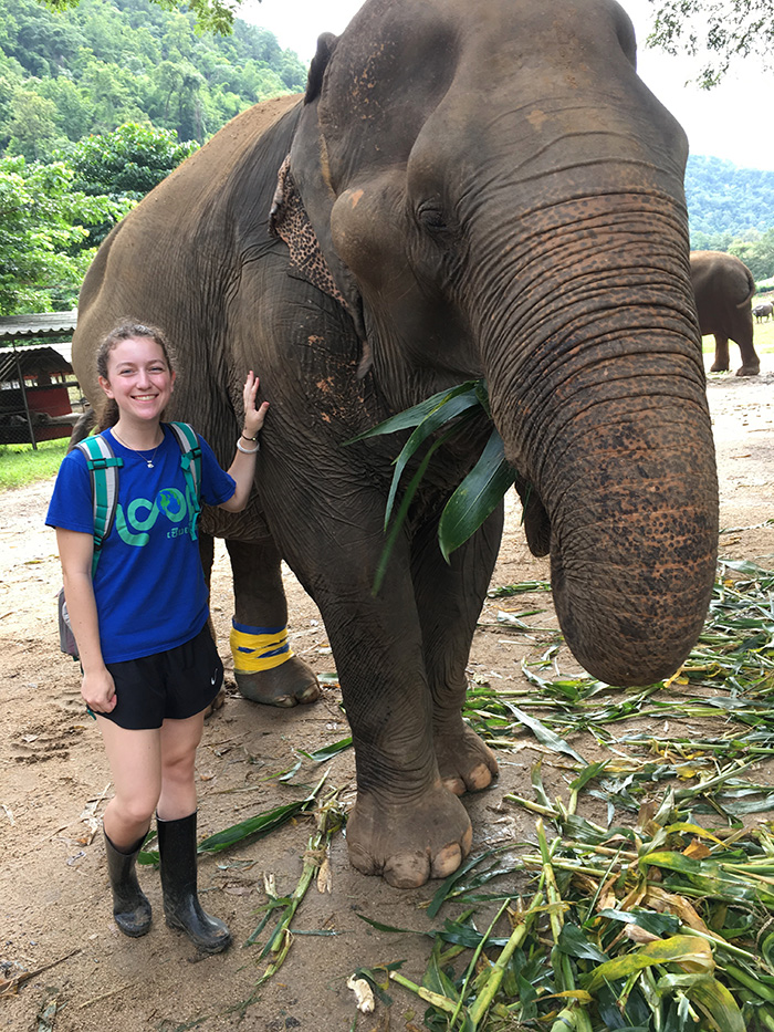 Chloe standing next to an elephant in a tropical location.