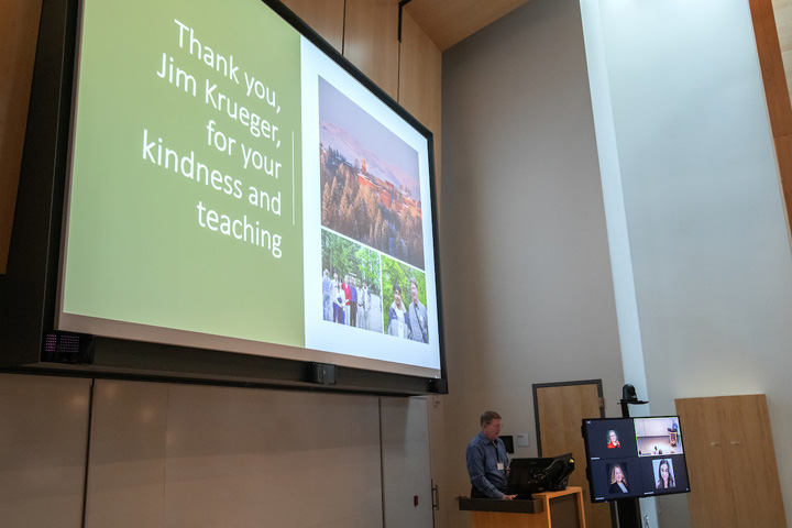 Wide angle shot of Dr. Krueger at the podium during his closing presentation, with a "Thank you, Jim Krueger for your kindness and teaching" slide behind him.