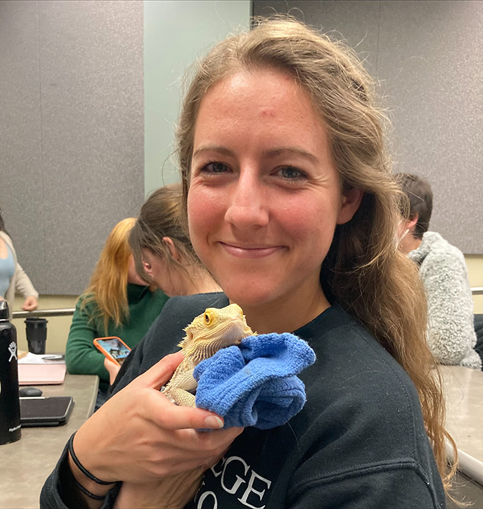 Montana is very happy to be holding a small yellow lizard in a classroom at the college.