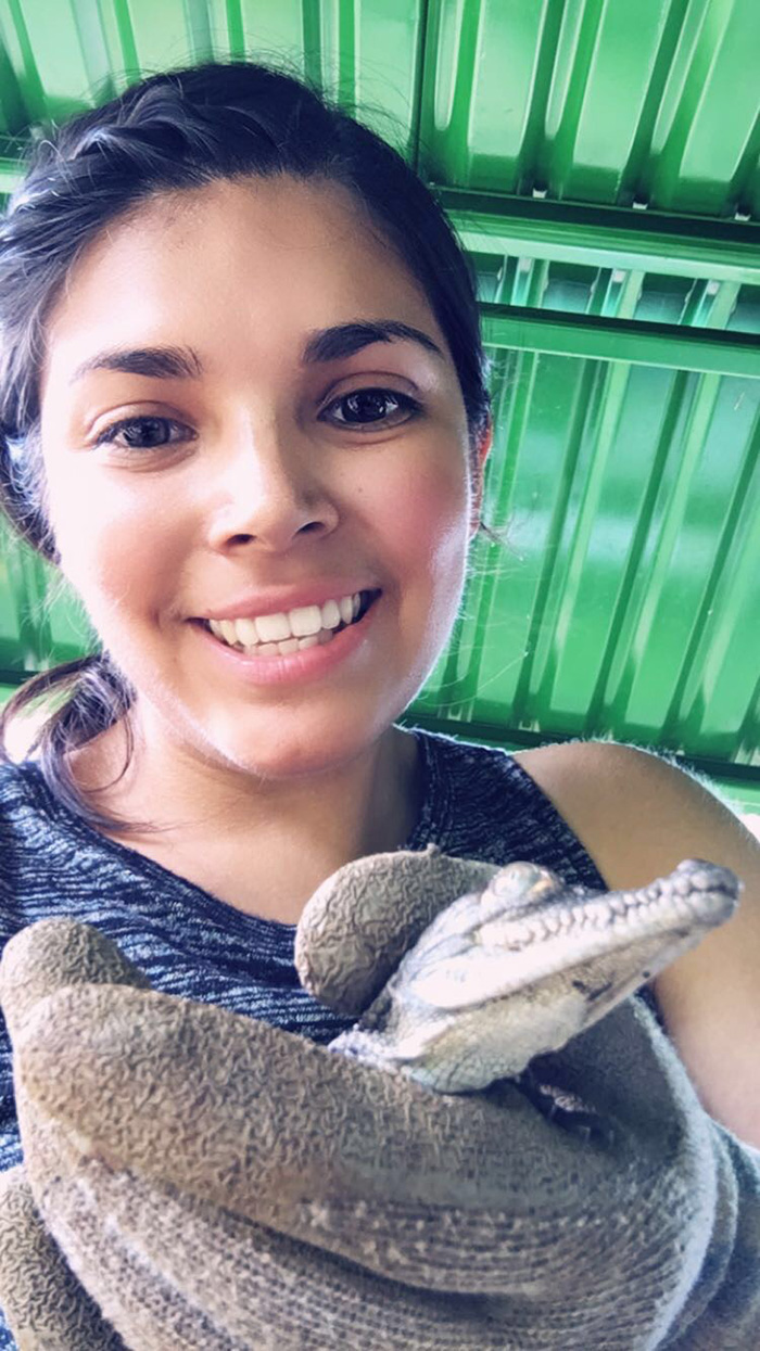 Close up image of Mirella while she is holding a small alligator. She is wearing protective gloves.