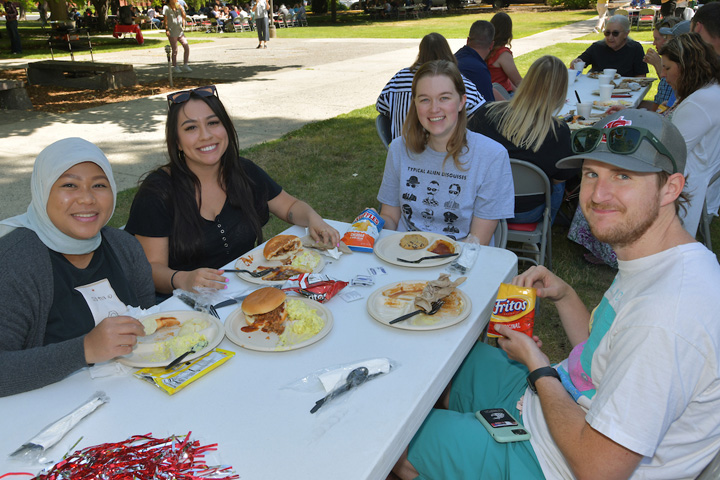 Group of co-workers eating at a table in the shade.