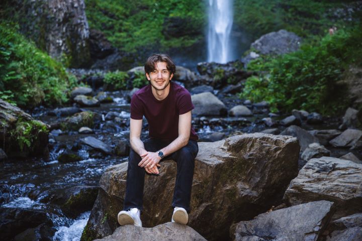 Scott Stevison sits on rocks in front of a waterfall.