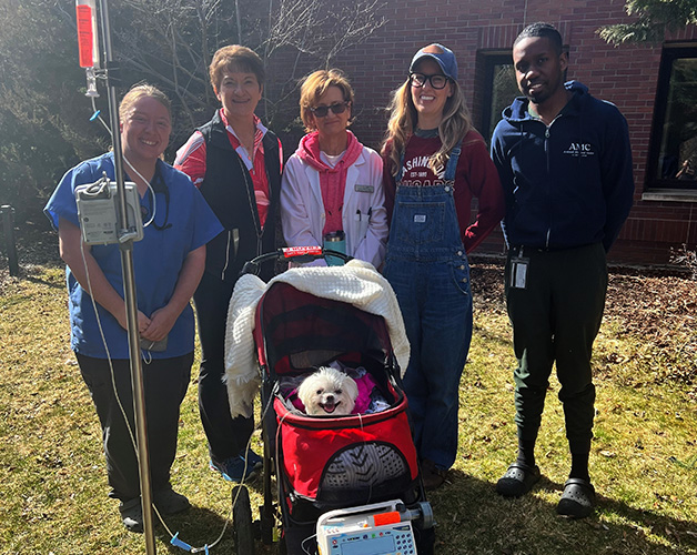 Mille in a stroller, outside the Teaching Hospital, with a group of caregivers around her. She is still attached to an IV.